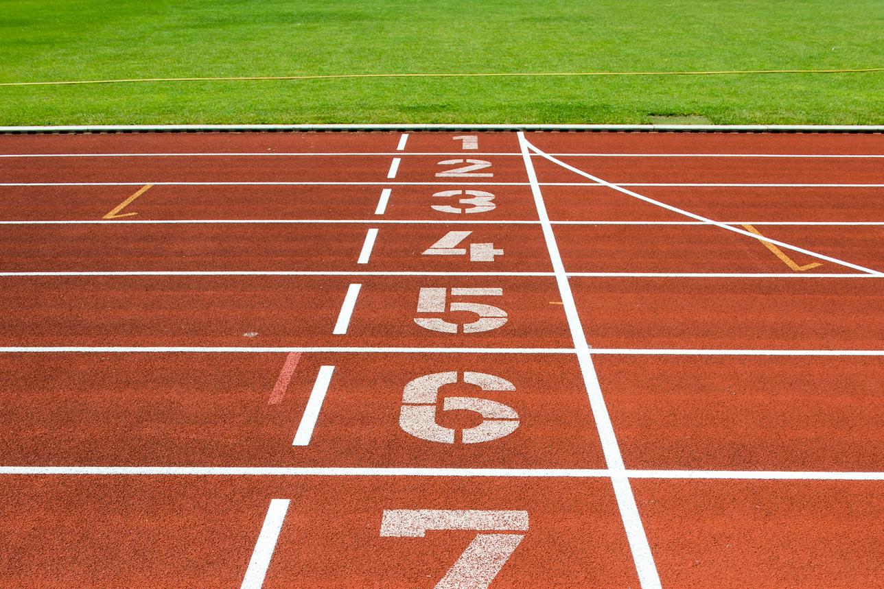 Nahaufnahme einer roten Laufbahn mit den Startnummern 1 bis 8 und grünem Rasen im Hintergrund.