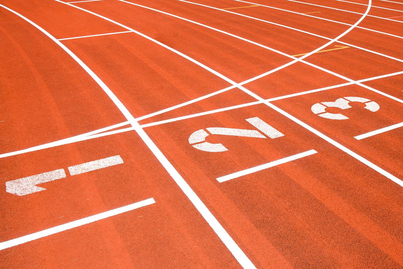 Nahaufnahme einer roten Laufbahn mit weißen Startnummern 1, 2, 3 und Markierungen für Laufstrecken.